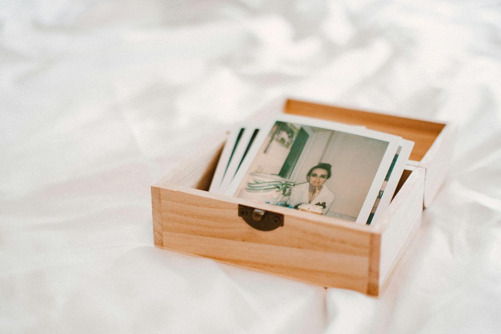 A wooden box holding vintage Polaroid photos on a soft white surface, evoking nostalgia.